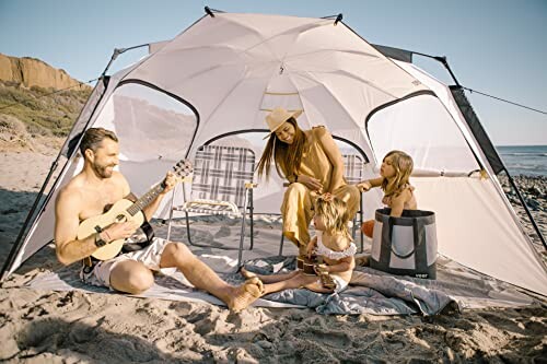 Family enjoying beach camping with a tent and playing music.